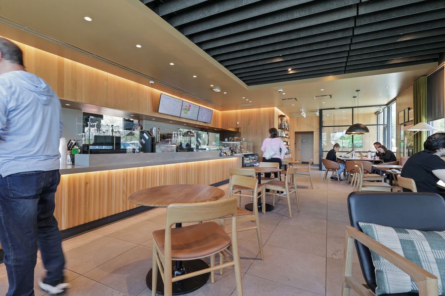 Spacious modern cafe interior with wood accents, natural light, and customers dining at tables near the counter.