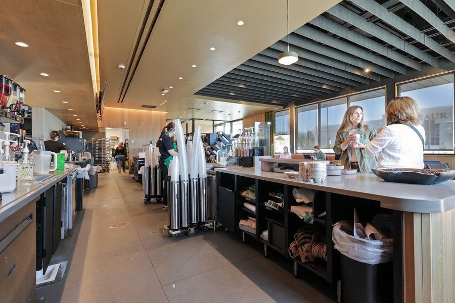 Modern coffee shop interior with baristas serving customers at a sleek counter with large windows and contemporary decor.