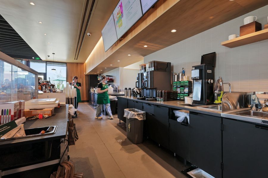 Modern coffee shop interior with baristas working behind a long counter with espresso machines and wood shelving.