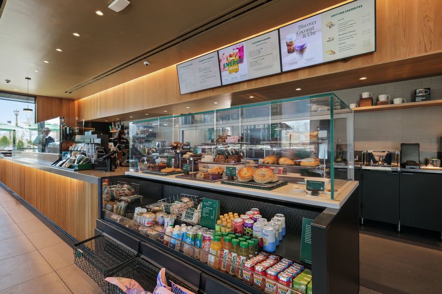 Starbucks cafe display case with pastries, packaged drinks, and digital menu boards above the counter.
