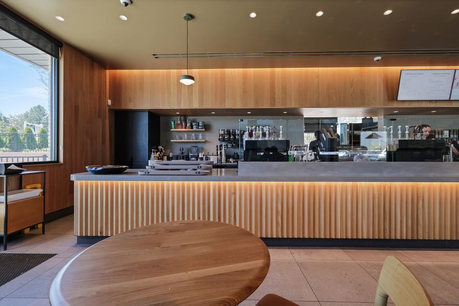 Modern cafe interior with warm wood paneling, sleek bar counter, pendant lighting, and large window view.