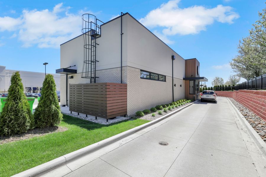 Modern commercial building with clean lines, brick accents, and lush landscaping along a paved driveway on a sunny day.