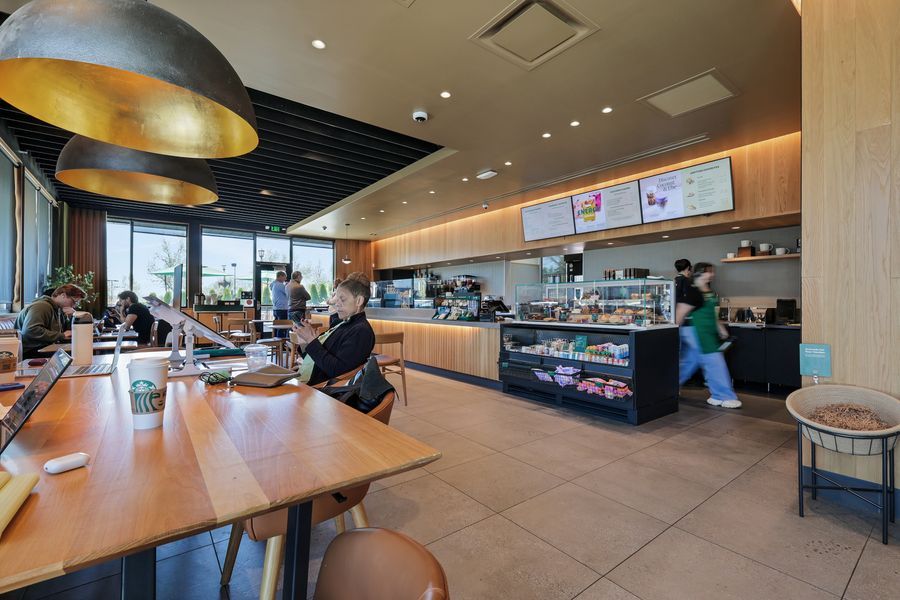 Modern Dunkin' Donuts interior with wooden tables, display counter, menu boards, and customers ordering at the service area.