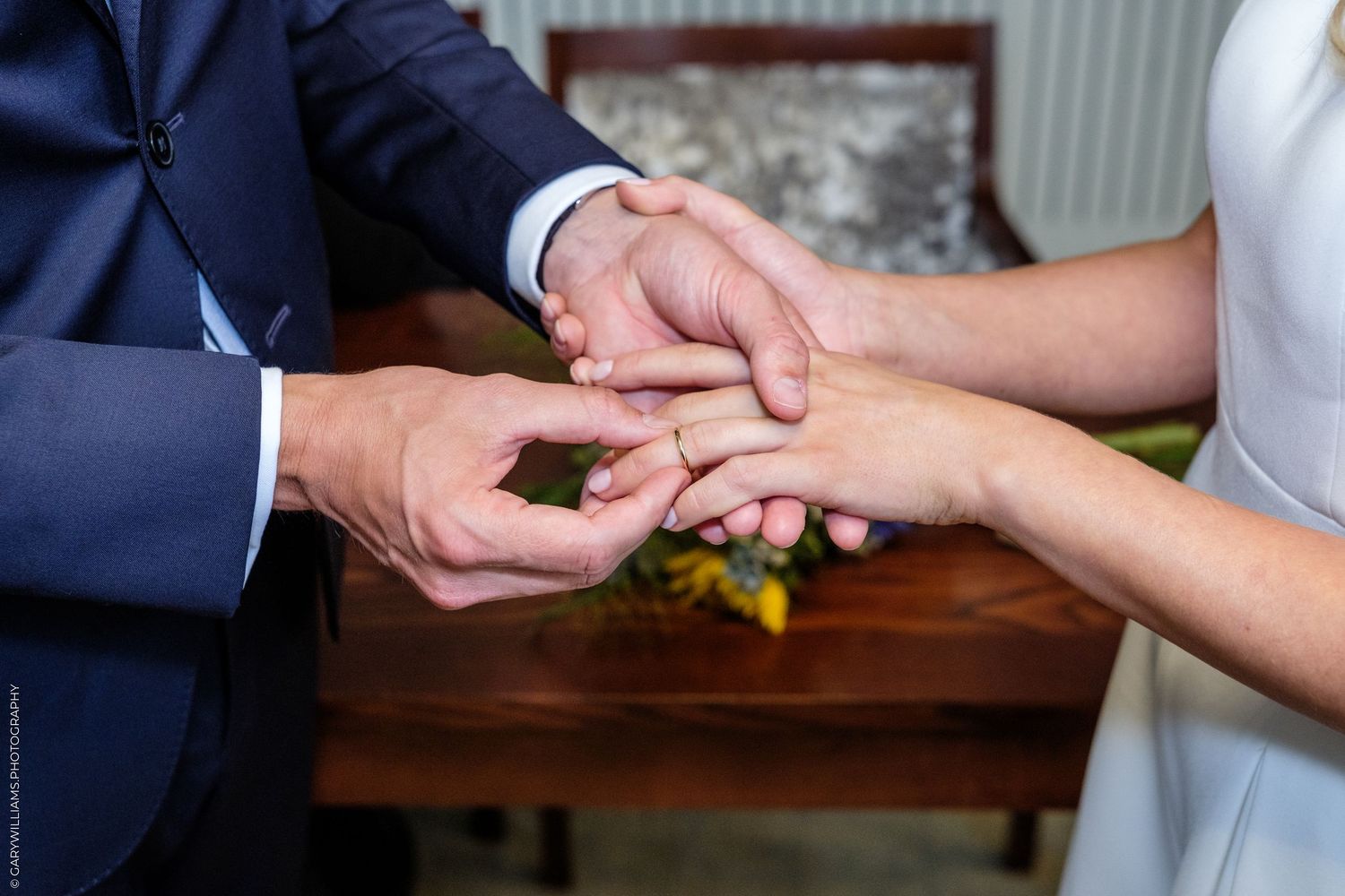 Groom placing a wedding ring on bride's finger during a ceremony, symbolizing love and commitment.