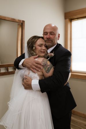 Emotional father-daughter embrace at wedding, bald man in black suit hugging bride in white gown and veil.