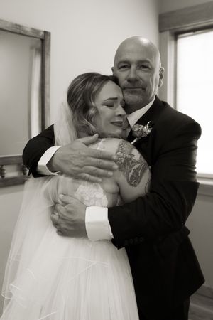 Black and white photo of a bald groom embracing a bride in a lace wedding dress and veil.