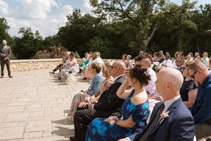 Wedding guests seated outdoors on stone patio during sunny ceremony celebration.