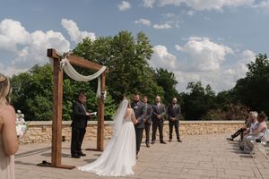 Bride walks toward groom at outdoor wedding altar with lake views and blue sky.