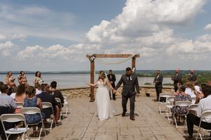 Newlywed couple walks joyfully down the aisle after their outdoor lakeside wedding ceremony.