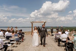 Bride and groom walk back down aisle after outdoor wedding ceremony by scenic lake.