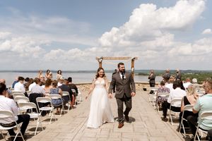 Newlyweds joyfully walk back down aisle after outdoor lakeside wedding ceremony.