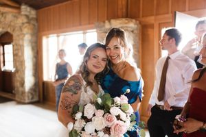 Smiling bride holding pink bouquet poses with a bridesmaid in a blue dress at wedding.
