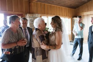 Bride in a lace wedding gown greets elderly and middle-aged female guests at an indoor wedding reception.