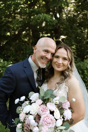 Smiling bride and groom pose together outdoors, bride holding pink and white rose bouquet with eucalyptus.