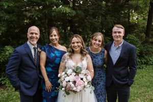 Wedding party of five poses outdoors in navy blue attire with bride holding pink and white floral bouquet.