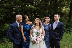 Wedding party of five smiling and laughing outdoors, bride in white gown holding pink bouquet.