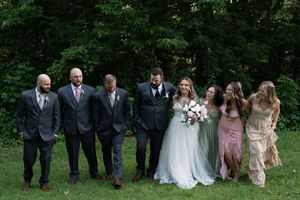 Wedding party walks together outdoors, groomsmen in gray suits and bridesmaids in sage green and floral dresses.
