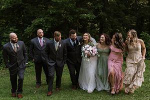 Wedding party walking together on grass, groomsmen in gray suits and bridesmaids in colorful gowns.