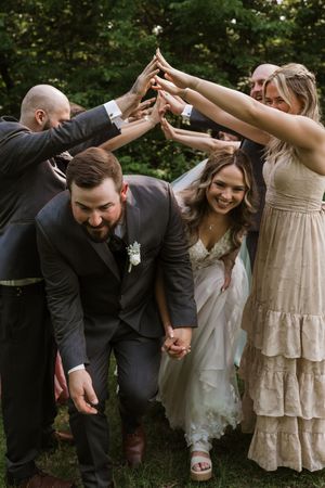 Wedding party forms arch with hands as bride and groom walk through laughing.