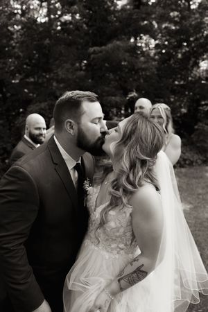 Black and white photo of bride and groom sharing first kiss after wedding ceremony outdoors.