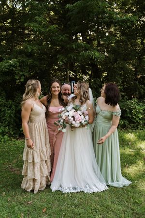 Groom playfully joins bride and three bridesmaids in pastel dresses for a fun outdoor photo.