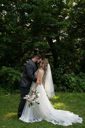 Bride and groom sharing a romantic kiss in a lush green garden, bride wearing a flowing white tulle gown with veil.