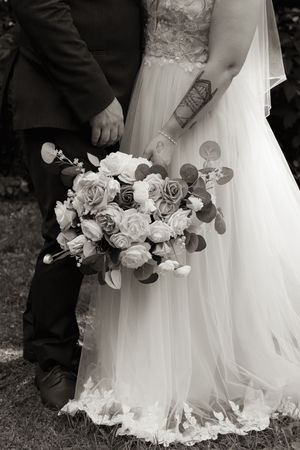 Black and white close-up of bride in lace gown and groom holding rose bouquet at wedding.