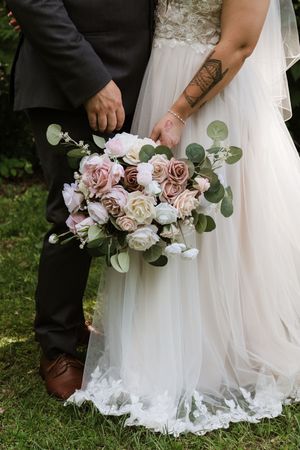 Close-up of bride and groom holding pink and white rose bouquet with eucalyptus greenery.