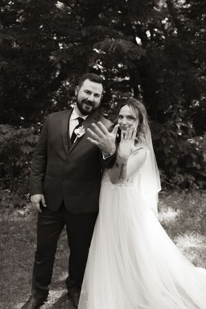 Newlyweds showing wedding rings to camera in black and white photo, bride in tulle gown.