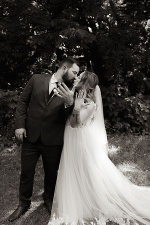 Black and white photo of bride and groom sharing a kiss outdoors on wedding day.