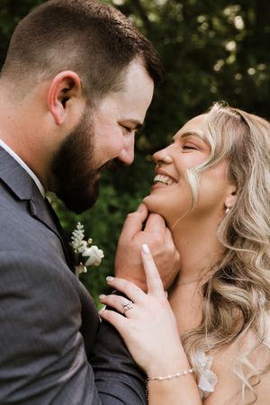 Groom tenderly holds brides chin as she smiles joyfully in close romantic portrait.
