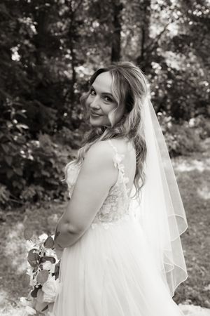 Black and white bridal portrait of smiling bride in lace gown and veil outdoors.