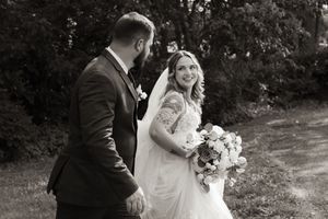 Black and white photo of bride and groom walking hand in hand outdoors.