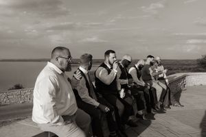 Black and white photo of groomsmen sitting on a wall overlooking a scenic waterfront.