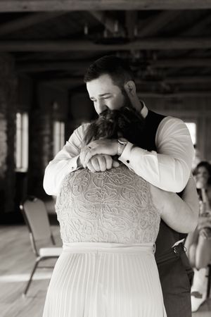 Groom tenderly embraces bride from behind during wedding dance in black and white photo.