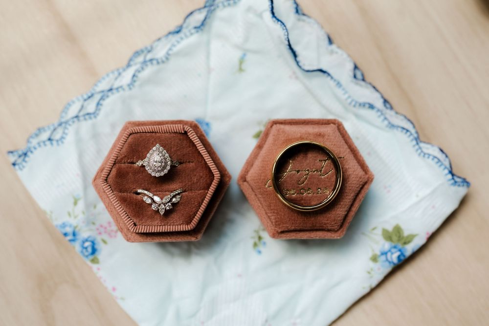Wedding rings displayed in a hexagonal velvet ring box on a floral handkerchief, featuring a diamond halo and gold band.