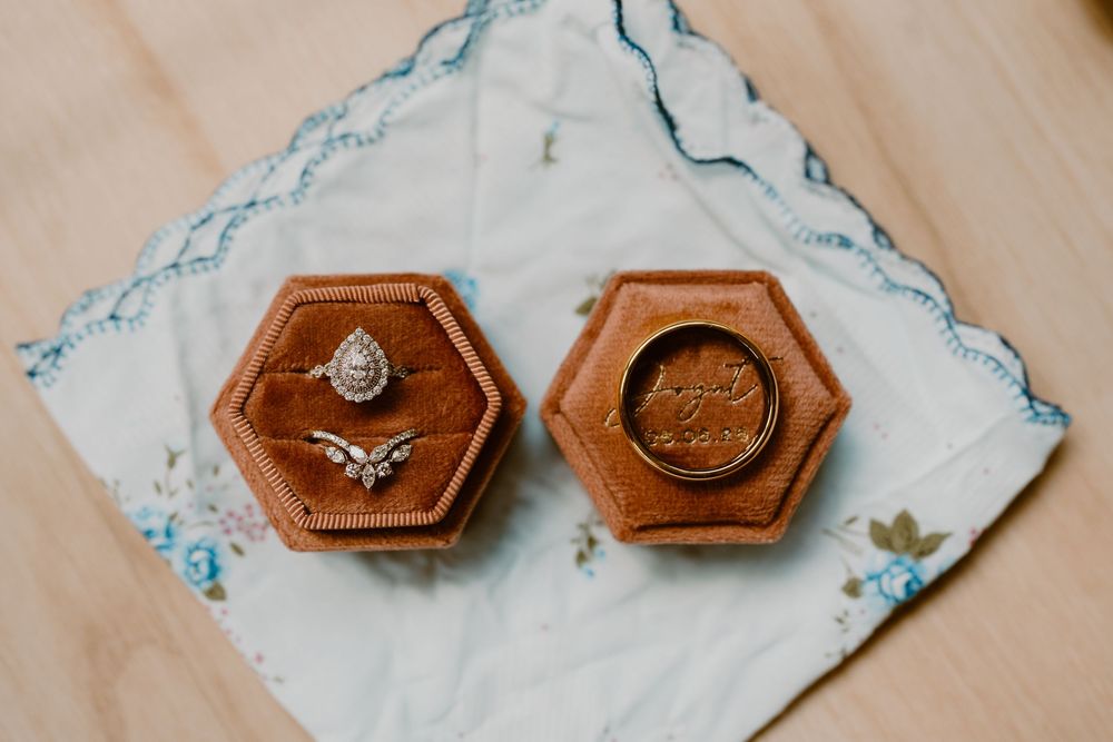 Wedding rings displayed in hexagonal velvet ring box on floral handkerchief on wooden surface.