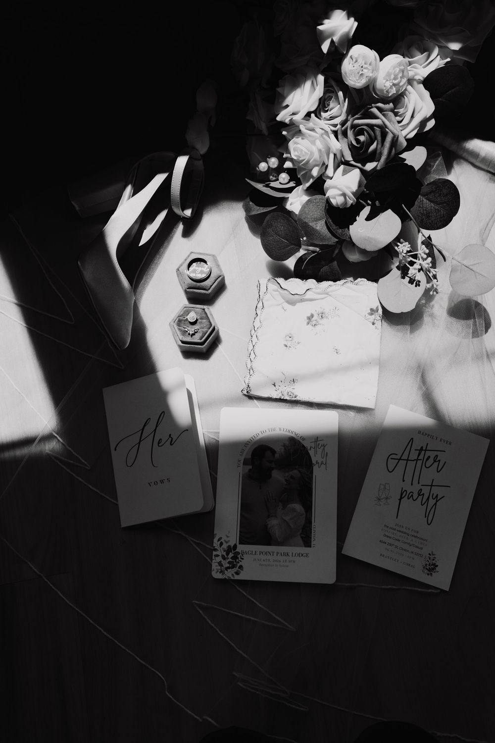 Black and white flat lay of wedding stationery, ring boxes, bouquet, and after party invitations.