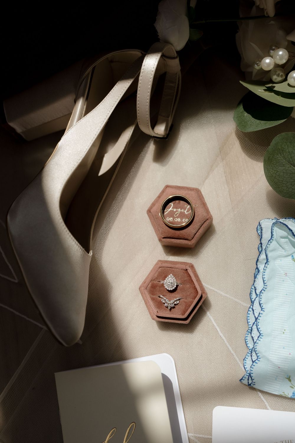 Wedding flat lay featuring diamond engagement ring, wedding band in hexagonal velvet box, bridal heels, and accessories.
