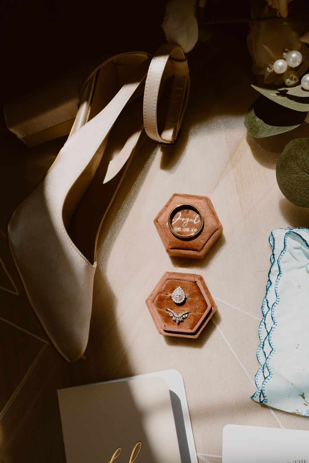 Close-up of wedding rings in hexagonal velvet box beside nude heels and blue embroidered handkerchief.