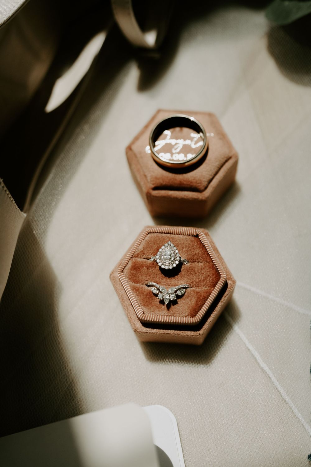 Close-up of elegant diamond engagement ring and wedding band displayed in velvet hexagon ring boxes.
