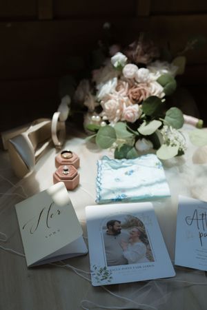 Wedding flat lay with rings, bouquet, vows cards, and couple photo on table.