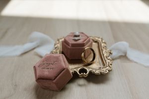 Pink velvet hexagon ring box and gold wedding band on ornate gold tray with white ribbon.