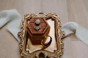 Elegant wedding rings displayed on gold ornate tray with velvet hexagon ring box and ribbon.
