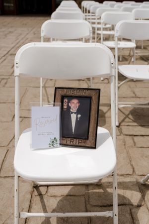 Memorial chair at wedding with framed photo of deceased loved one in fishing-themed frame and reserved sign.