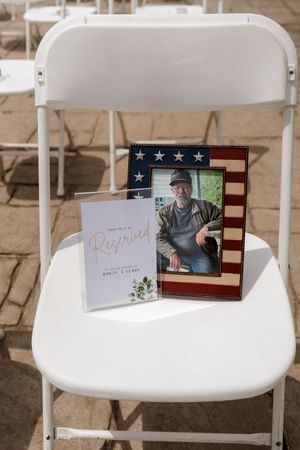 Reserved memorial chair with American flag framed photo honoring a loved one at an outdoor wedding ceremony.