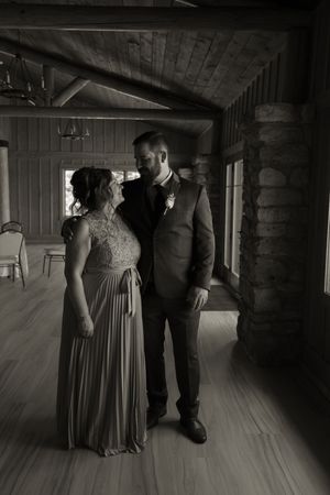 Black and white photo of a couple sharing a tender moment inside a rustic log cabin wedding venue.