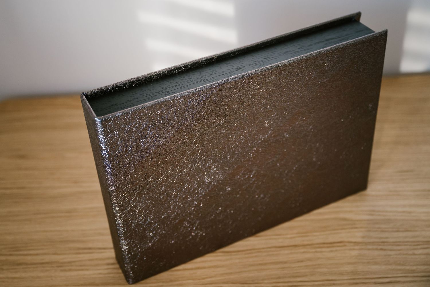 Dark brown textured hardcover book standing upright on a wooden surface with metallic speckled finish.