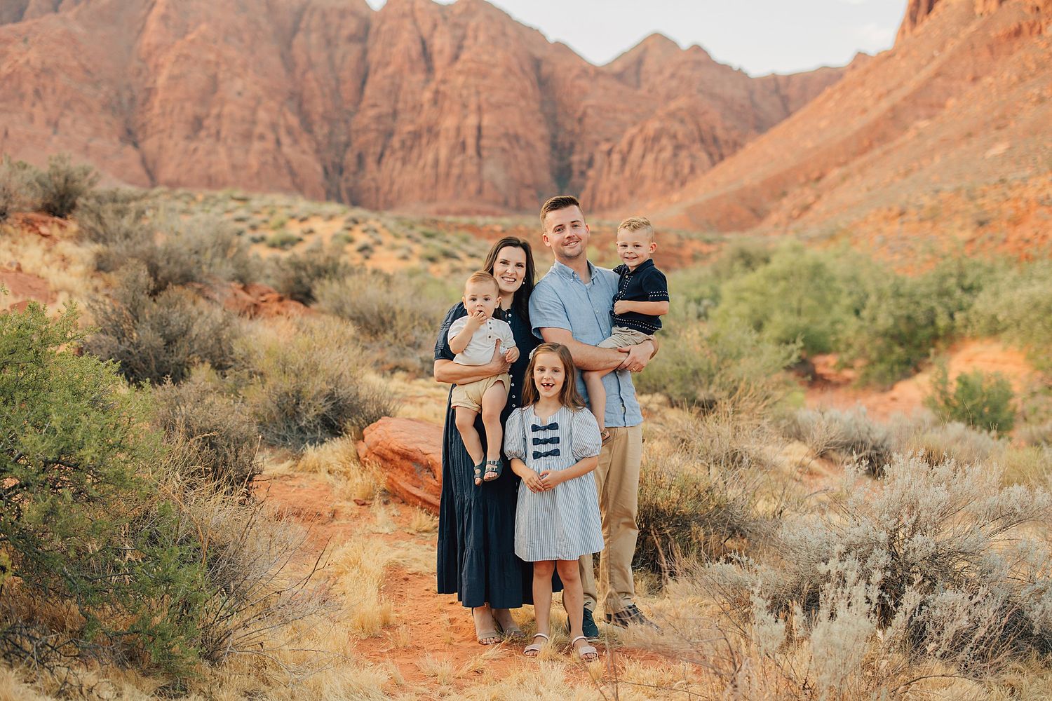 Family of five posing in red rock desert landscape with rustic canyon backdrop during golden hour photography session.