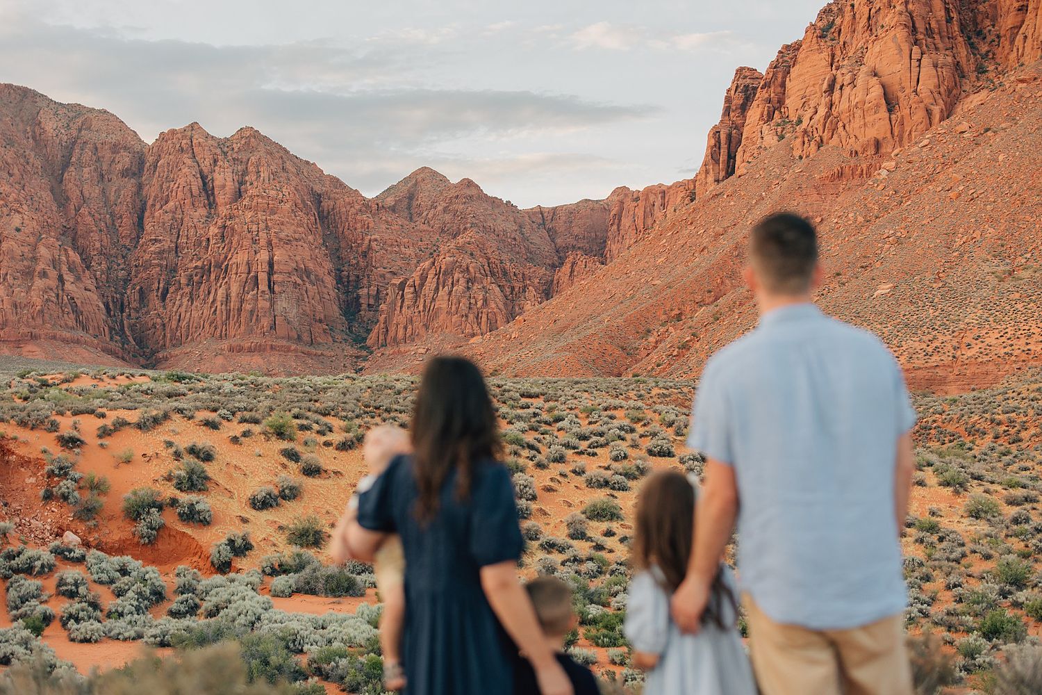 Family of three admiring stunning red rock canyon landscape in the desert at sunset.